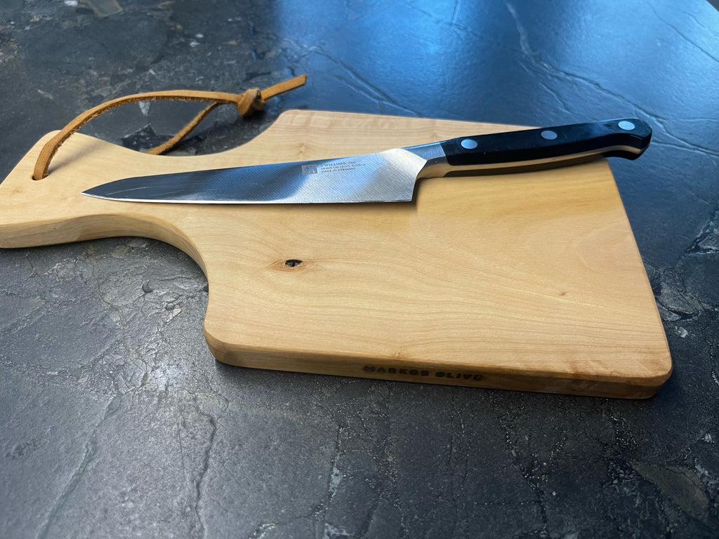 Olivenholz-Schneidebrett von MARKOS OLIVE mit hochwertigem Küchenmesser auf dunkler Steinplatte – natürliches Design und edle Verarbeitung.
