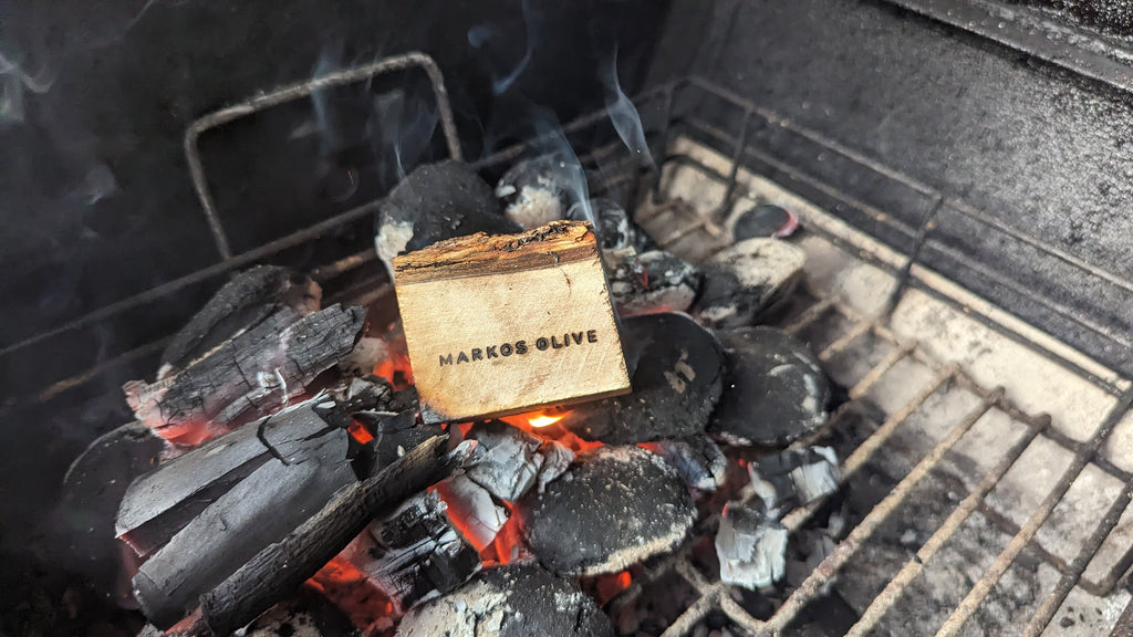 Olivenholz-Smoking Chunk von MARKOS OLIVE auf heißer Grillglut, beginnt zu rauchen – BBQ-Aroma pur_MARKOS OLIVE Smoking Chunk im Einsatz