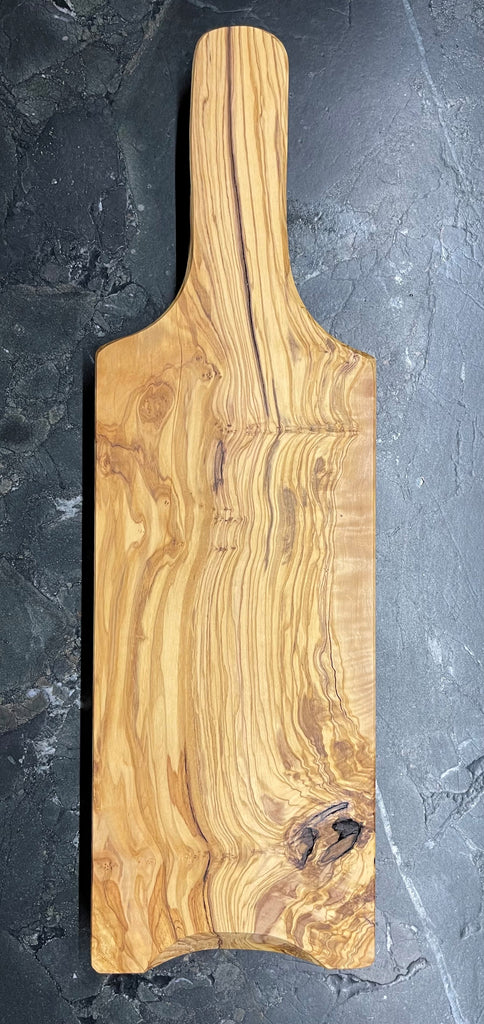 Seitliche Ansicht eines handgefertigten Schneidebretts aus massivem Olivenholz mit ergonomischem Griff, sanft abgerundeten Kanten und markanter Maserung – präsentiert auf dunklem Naturstein.