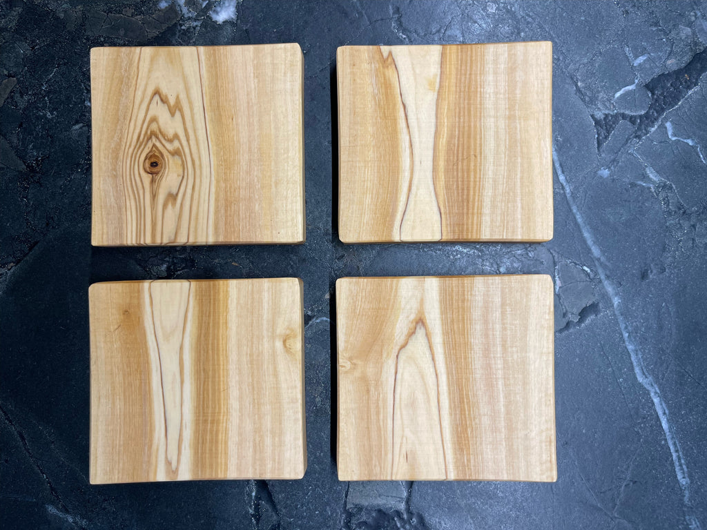 Vier quadratische Untersetzer aus edlem Olivenholz, jede mit einzigartiger Maserung und warmem Farbton. Auf dunklem Steinuntergrund präsentiert, bringen sie mediterranen Charme und handwerkliche Qualität auf jeden Tisch. Ideal für Gläser, Tassen oder kleine Servierideen.