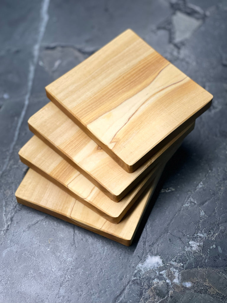 Vier quadratische Untersetzer aus edlem Olivenholz, jede mit einzigartiger Maserung und warmem Farbton. Auf dunklem Steinuntergrund präsentiert, bringen sie mediterranen Charme und handwerkliche Qualität auf jeden Tisch. Ideal für Gläser, Tassen oder kleine Servierideen.