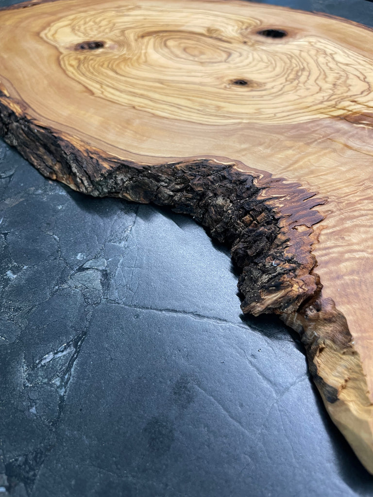 Olivenholz-Servierbrett mit markkante Rinde, fotografiert auf eine schwarze Steinplatte