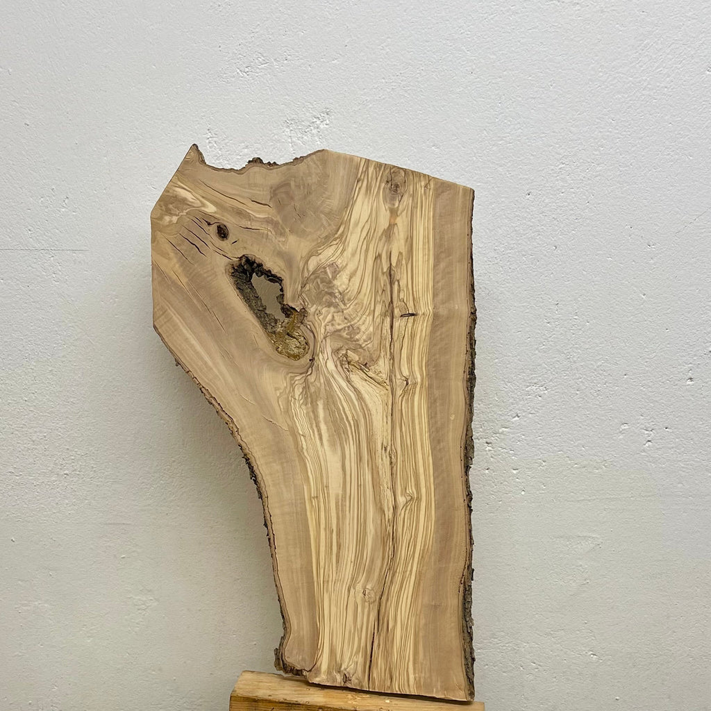 Ganzaufnahme eines Olivenholzbretts mit Naturkante, markanter Maserung und gewachsenem Loch mit teilweise abgebauter Holzsubstanz.