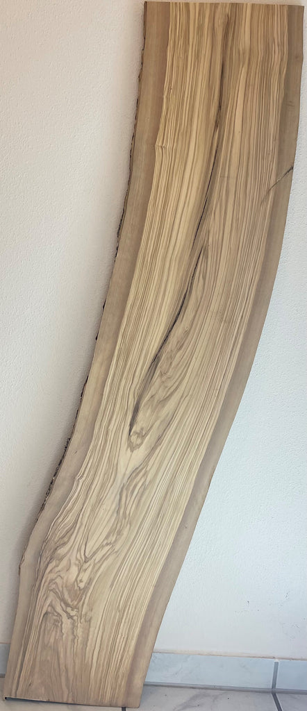 Gebogenes Olivenholzbrett mit naturbelassener Rinde und lebendiger Maserung, aufrecht an Wand gelehnt