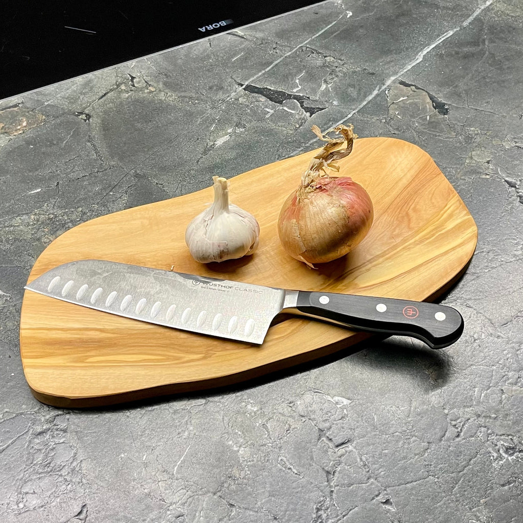 Schneidebrett S475 mit Messer, Knoblauch und Zwiebel auf dunkler Steinplatte – mediterrane Atmosphäre.
