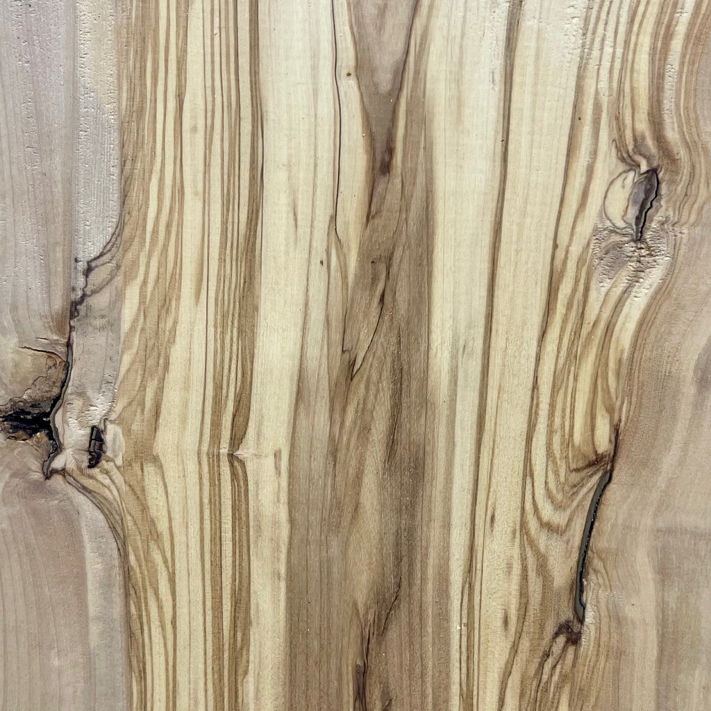Nahaufnahme eines natürlichen Astlochs mit dunkler Einfärbung – umgeben von welliger, kontrastreicher Maserung im Kernbereich der Olivenholzbohle.