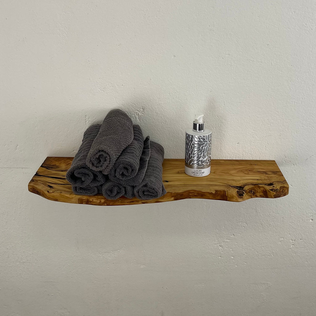 Kompaktes Wandboard aus Olivenholz mit unregelmäßiger Naturkante und ausdrucksstarker Maserung, dekoriert mit grauen Handtüchern und Seifenspender.