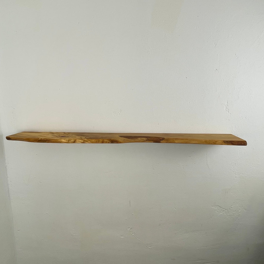 Schwebendes Regalbrett aus massivem Olivenholz mit charaktervoller Naturkante, klarer Linienführung und markanter Maserung – an weißer Wand montiert.