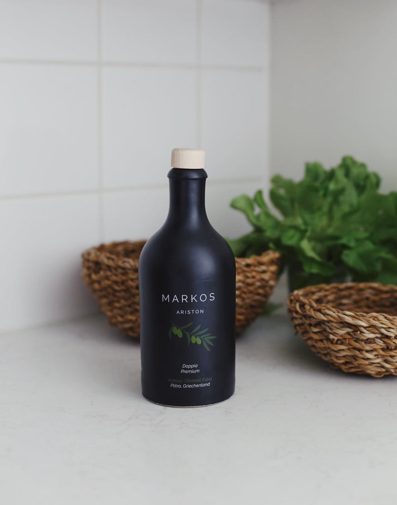 Eine Steinzeugflasche mit MARKOS OLIVE PREMIUM OLIVENOEL steht auf eine Küchen-Arbeitsplatte